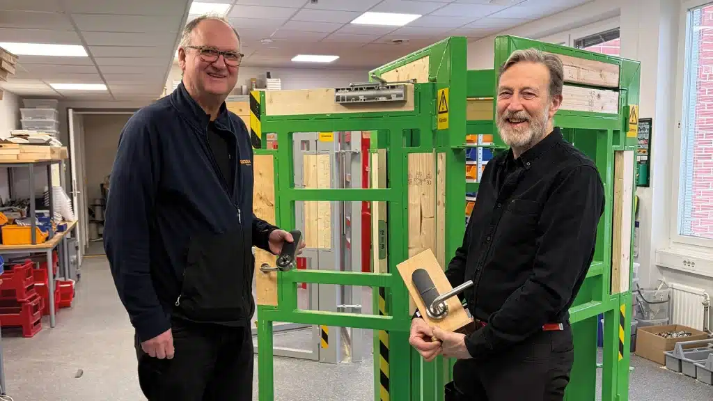 Två manliga lärare på Praktiska gymnasiet står leende framför en grön metallkonstruktion.